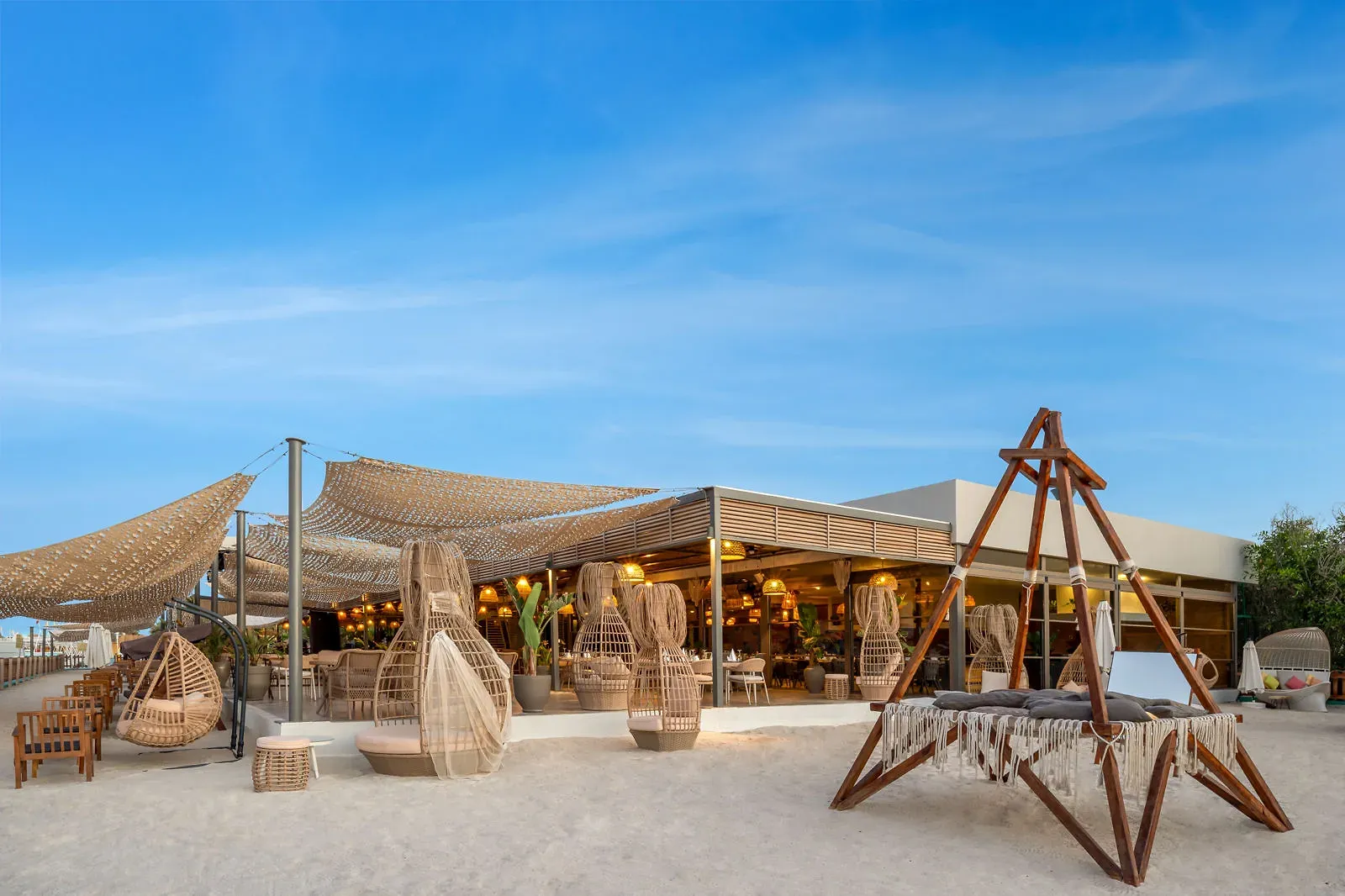 Loungeplek op het strand van Delphin Be Grand met hangstoelen, een houten schommel en schaduwdoeken